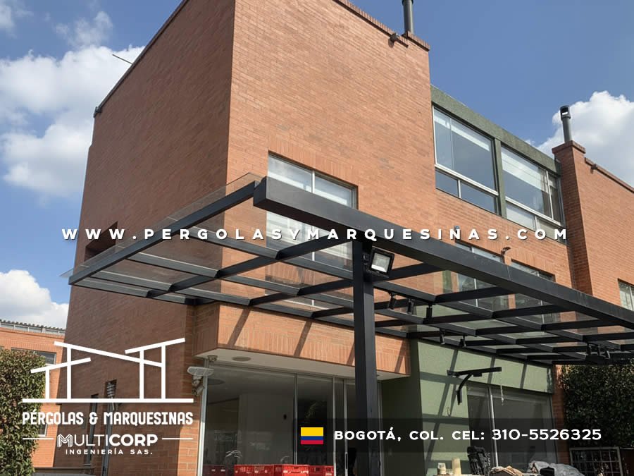 Pérgola metálica negra con techo de vidrio templado para acceso residencial en Bogotá, Colombia. Multicorp Ingeniería SAS.