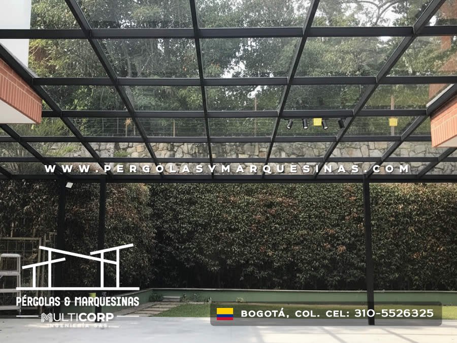Pérgola de vidrio con estructura metálica negra sobre jardín de conjunto residencial en Bogotá, Colombia. Multicorp Ingeniería SAS.