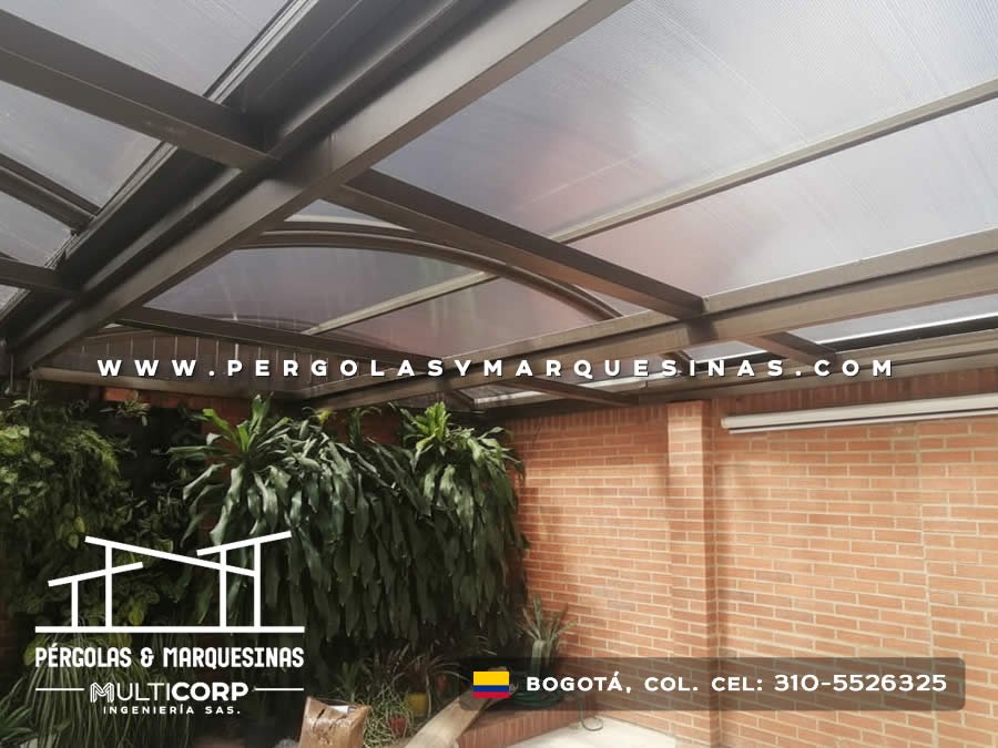 Techo de policarbonato translúcido con vigas metálicas curvas y jardinera en patio de vivienda en Bogotá, Colombia. Multicorp Ingeniería SAS.