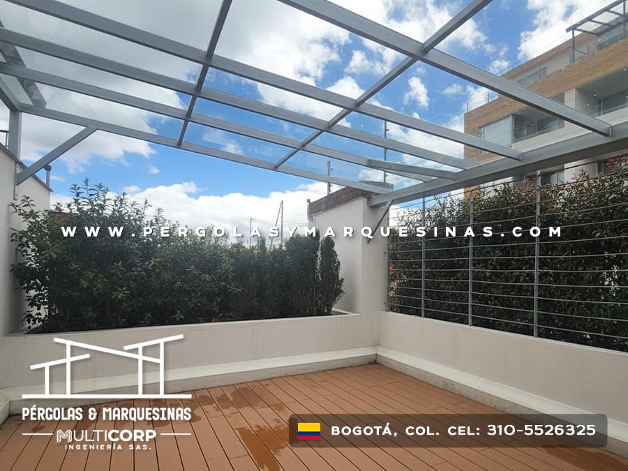 Pérgola de vidrio templado con estructura gris sobre terraza con deck de madera en Bogotá, Colombia. Multicorp Ingeniería SAS.
