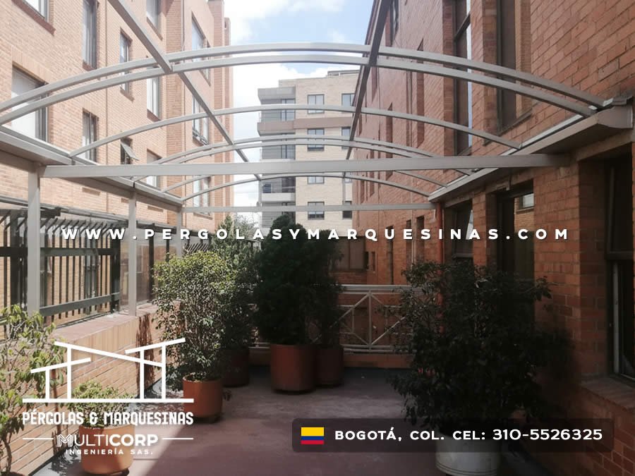 Estructura curva de policarbonato translúcido sobre patio con jardín entre edificios en Bogotá, Colombia. Multicorp Ingeniería SAS.