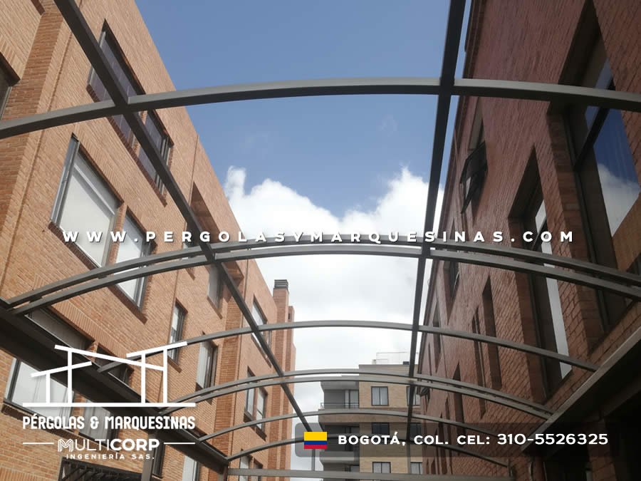 Cubierta curva translúcida con estructura metálica oscura, conectando edificios residenciales en Bogotá, Colombia. Multicorp Ingeniería SAS.