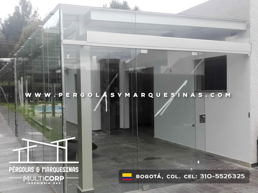 Marquesina de vidrio con estructura blanca y cerramiento lateral transparente en vivienda moderna en Bogotá, Colombia. Multicorp Ingeniería SAS.
