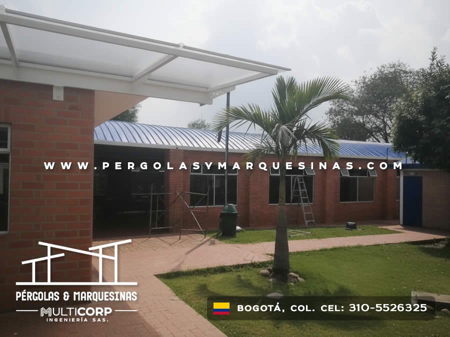 Cubierta translúcida con perfiles blancos sobre corredor exterior de edificio escolar con jardín en Bogotá, Colombia. Multicorp Ingeniería SAS. Cubierta translúcida con perfiles blancos sobre corredor exterior de edificio escolar con jardín en Bogotá, Colombia. Multicorp Ingeniería SAS.