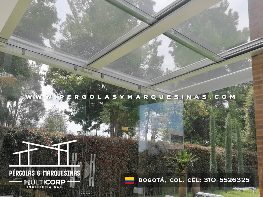 Estructura de cristal con perfiles blancos sobre patio con vista a jardín arbolado en casa de Bogotá, Colombia. Multicorp Ingeniería SAS. Estructura de cristal con perfiles blancos sobre patio con vista a jardín arbolado en casa de Bogotá, Colombia. Multicorp Ingeniería SAS.