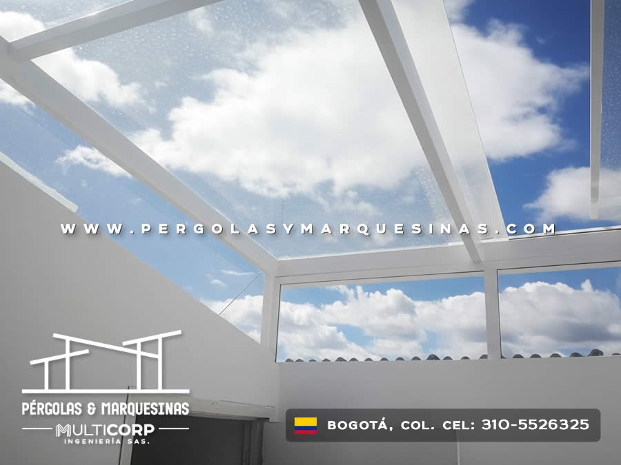 Techo de vidrio transparente con vigas blancas sobre terraza interior con paredes blancas y cielo visible en Bogotá, Colombia. Multicorp Ingeniería SAS. Techo de vidrio transparente con vigas blancas sobre terraza interior con paredes blancas y cielo visible en Bogotá, Colombia. Multicorp Ingeniería SAS.