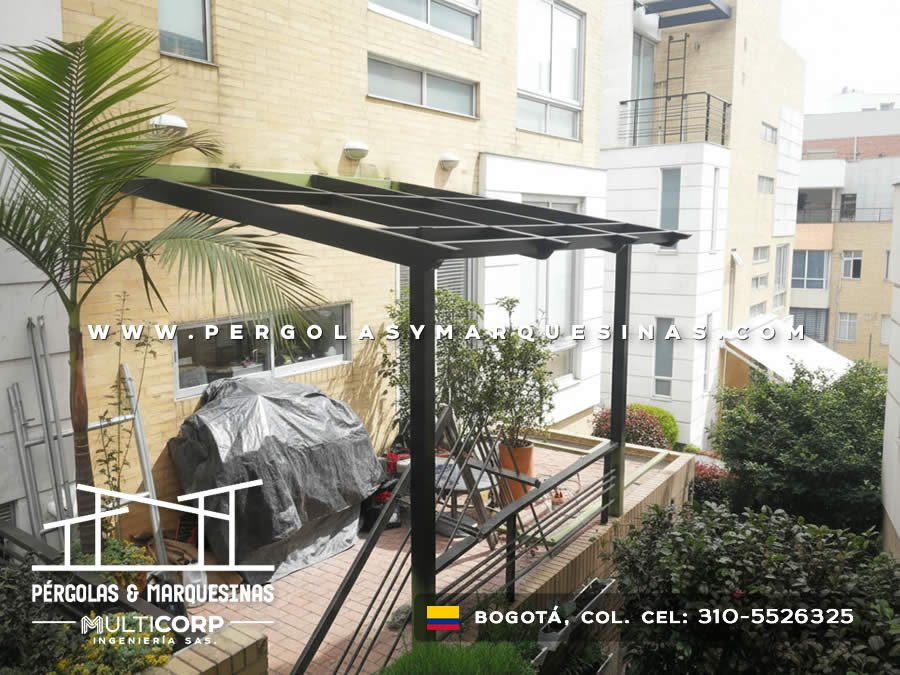 Pergola metalica negra con techo policarbonato sobre terraza jardin edificio residencial con palmera en Bogotá, Colombia. Multicorp Ingeniería SAS. Pergola metalica negra con techo policarbonato sobre terraza jardin edificio residencial con palmera en Bogotá, Colombia. Multicorp Ingeniería SAS.