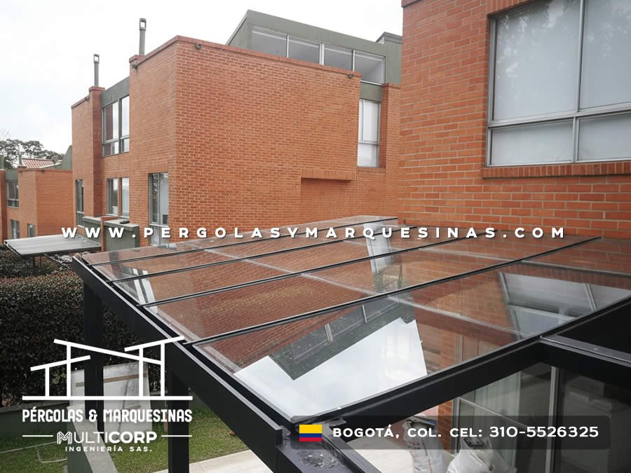 Pergola acristalada metalica negra techo vidrio transparente sobre patio edificio ladrillo rojo con cesped en Bogotá, Colombia. Multicorp Ingeniería SAS. Pergola acristalada metalica negra techo vidrio transparente sobre patio edificio ladrillo rojo con cesped en Bogotá, Colombia. Multicorp Ingeniería SAS.