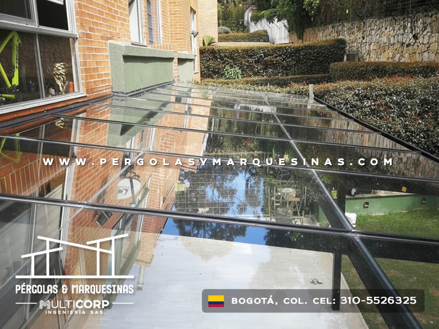 Pergola acristalada metalica negra techo vidrio sobre jardin cesped edificio ladrillo rojo con vegetacion en Bogotá, Colombia. Multicorp Ingeniería SAS. Pergola acristalada metalica negra techo vidrio sobre jardin cesped edificio ladrillo rojo con vegetacion en Bogotá, Colombia. Multicorp Ingeniería SAS.