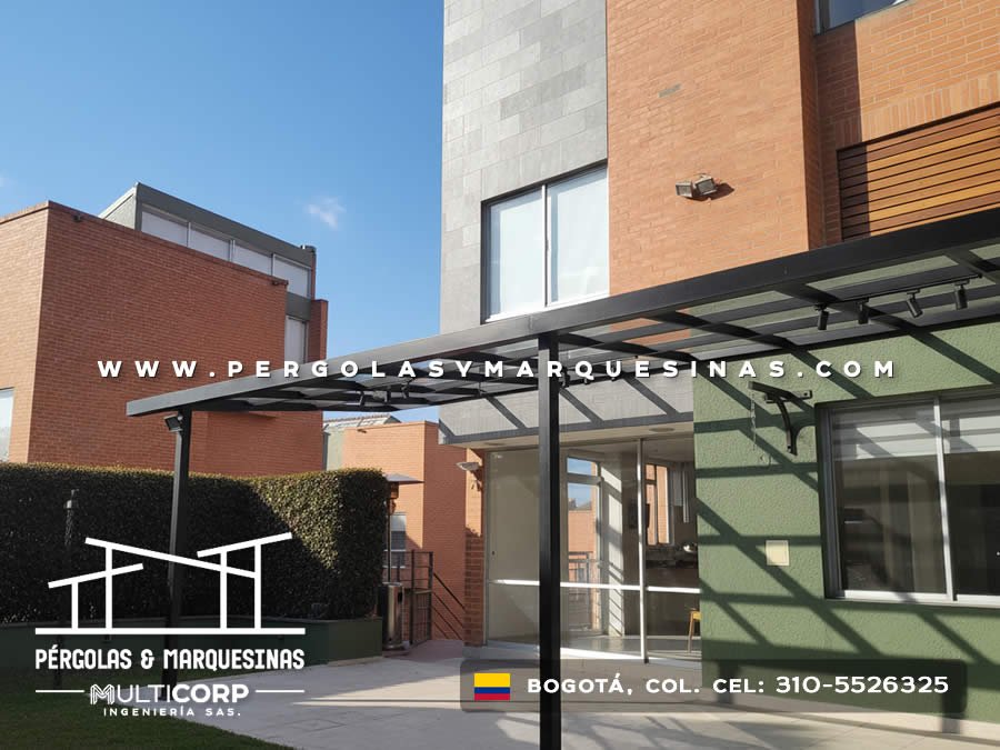 Pergola metalica negra techo policarbonato sobre terraza jardin edificio ladrillo rojo con pared verde y edificios al fondo en Bogotá, Colombia. Multicorp Ingeniería SAS. Pergola metalica negra techo policarbonato sobre terraza jardin edificio ladrillo rojo con pared verde y edificios al fondo en Bogotá, Colombia. Multicorp Ingeniería SAS.