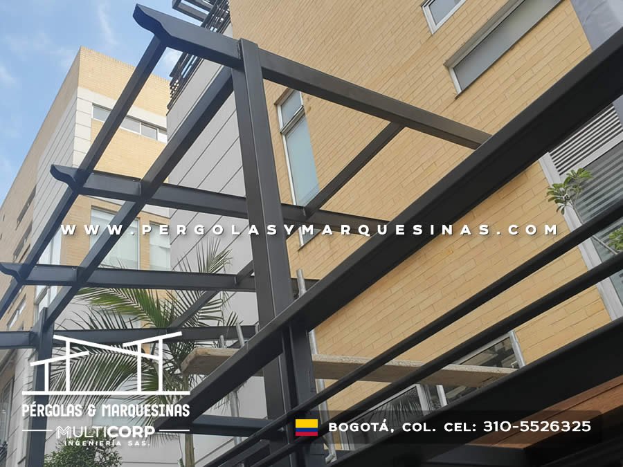 Pergola metalica negra estructura abierta con perfiles sobre terraza edificio ladrillo amarillo con palmera en Bogotá, Colombia. Multicorp Ingeniería SAS. Pergola metalica negra estructura abierta con perfiles sobre terraza edificio ladrillo amarillo con palmera en Bogotá, Colombia. Multicorp Ingeniería SAS.
