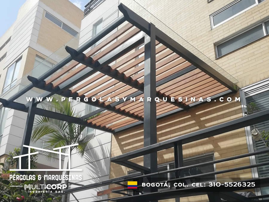 Pergola metalica negra con lamas de madera sobre terraza edificio ladrillo amarillo con palmera y baranda en Bogotá, Colombia. Multicorp Ingeniería SAS. Pergola metalica negra con lamas de madera sobre terraza edificio ladrillo amarillo con palmera y baranda en Bogotá, Colombia. Multicorp Ingeniería SAS.
