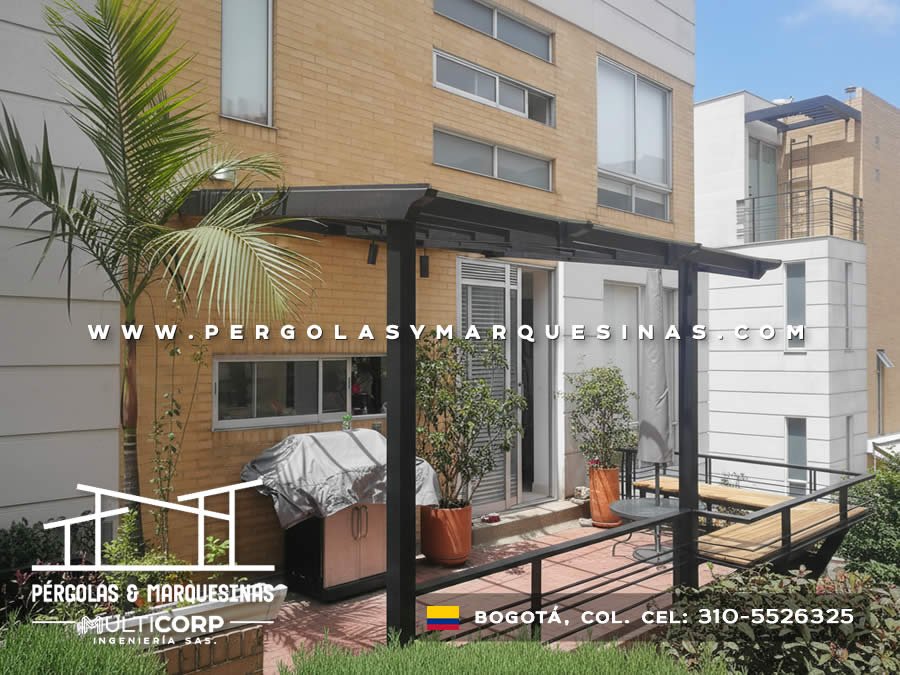 Pergola metalica negra techo policarbonato sobre jardin terraza edificio ladrillo amarillo con palmera y muebles en Bogotá, Colombia. Multicorp Ingeniería SAS. Pergola metalica negra techo policarbonato sobre jardin terraza edificio ladrillo amarillo con palmera y muebles en Bogotá, Colombia. Multicorp Ingeniería SAS.