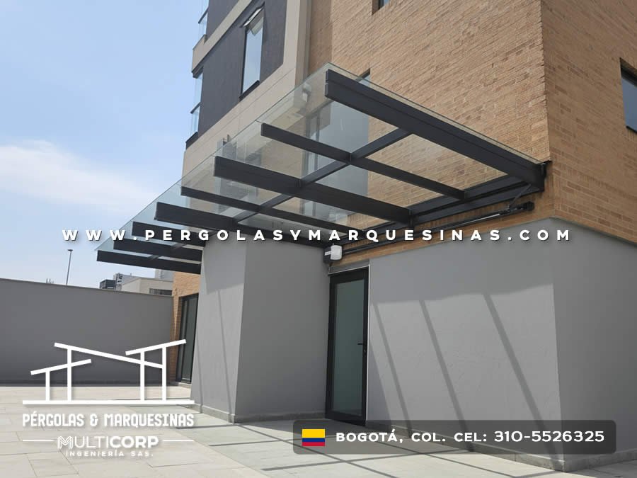 Marquesina acristalada metalica negra techo vidrio sobre entrada edificio con pared gris y puerta moderna en Bogotá, Colombia. Multicorp Ingeniería SAS. Marquesina acristalada metalica negra techo vidrio sobre entrada edificio con pared gris y puerta moderna en Bogotá, Colombia. Multicorp Ingeniería SAS.
