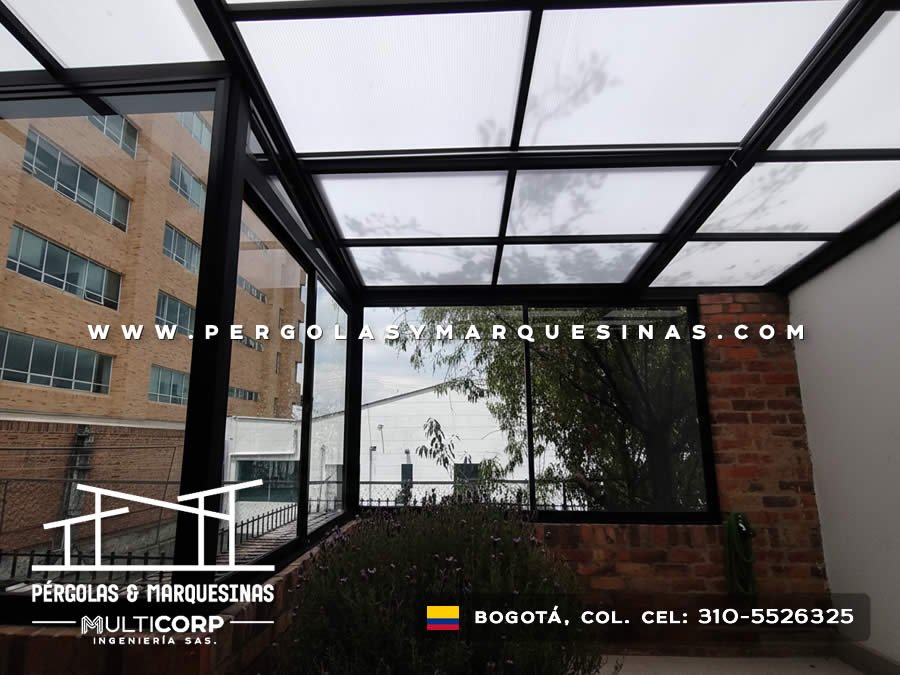 Techo de policarbonato con estructura de aluminio negro sobre patio residencial con vista a edificios en Bogotá, Colombia. Multicorp Ingeniería SAS.