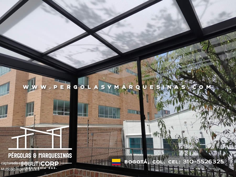Cubierta de policarbonato con perfileria negra sobre patio residencial con vegetacion y edificios circundantes en Bogotá, Colombia. Multicorp Ingeniería SAS.