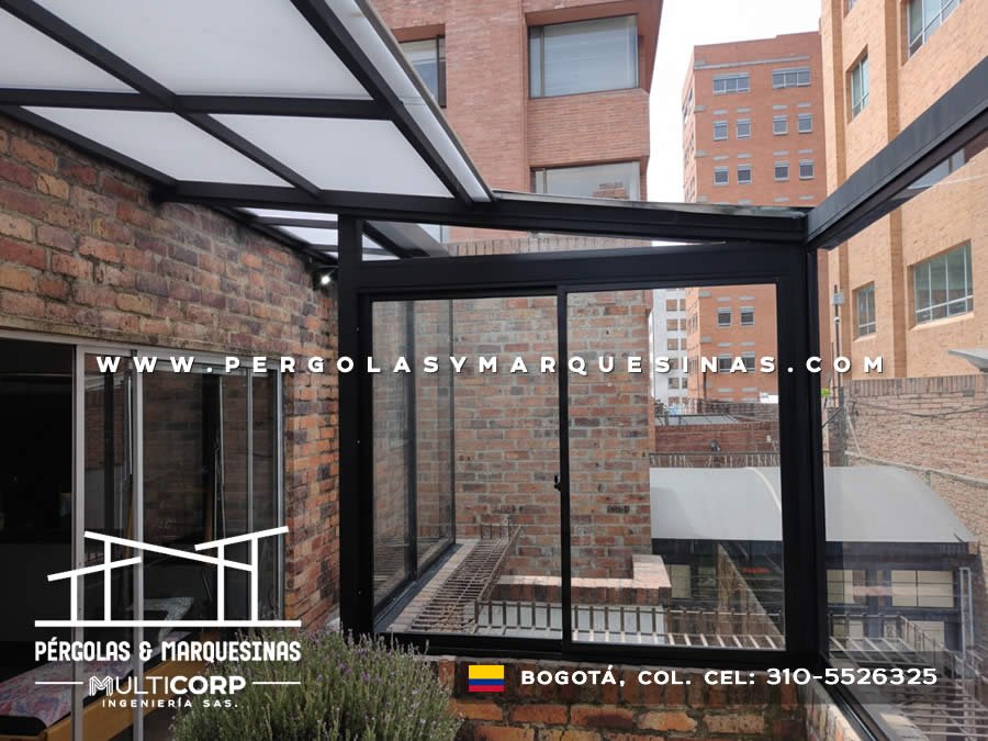 Cubierta de vidrio y aluminio negro con ventanas corredizas sobre terraza residencial con edificios urbanos en Bogotá, Colombia. Multicorp Ingeniería SAS.