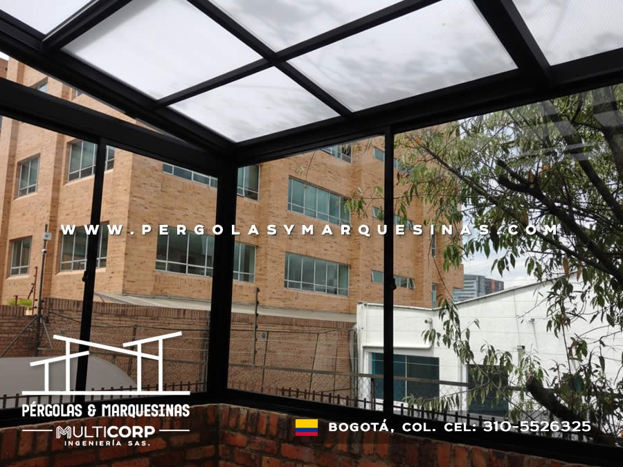 Estructura metalica negra con cubierta translucida y ventanas de vidrio sobre balcon con vista a edificios residenciales en Bogotá, Colombia. Multicorp Ingeniería SAS.