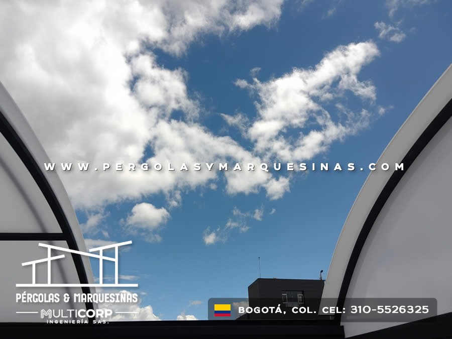 Vista cenital de estructura metalica curva con policarbonato translucido abierta hacia cielo azul con nubes en Bogotá, Colombia. Multicorp Ingeniería SAS.