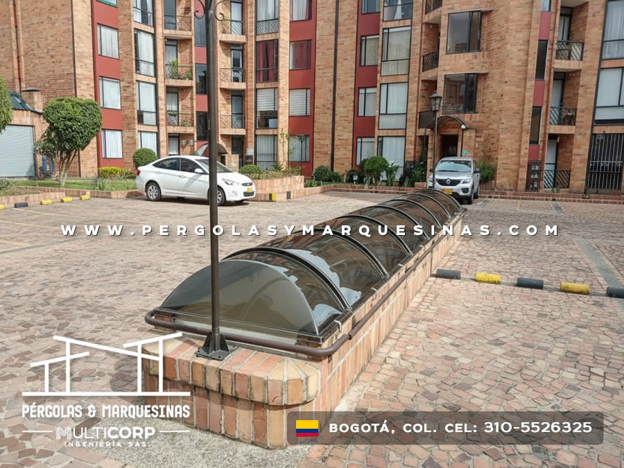 Domos curvos de policarbonato con estructura metalica sobre tragaluces de conjunto residencial con vehiculos en Bogotá, Colombia. Multicorp Ingeniería SAS.