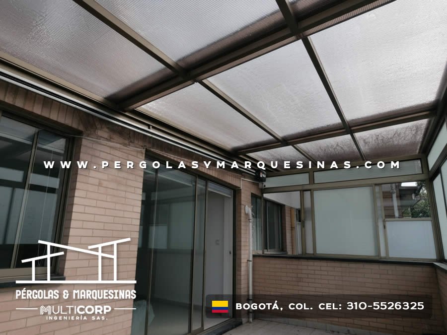 Cubierta de policarbonato con estructura de aluminio oscuro en terraza de casa con puerta corrediza y muro de ladrillo en Bogotá, Colombia. Multicorp Ingeniería SAS.
