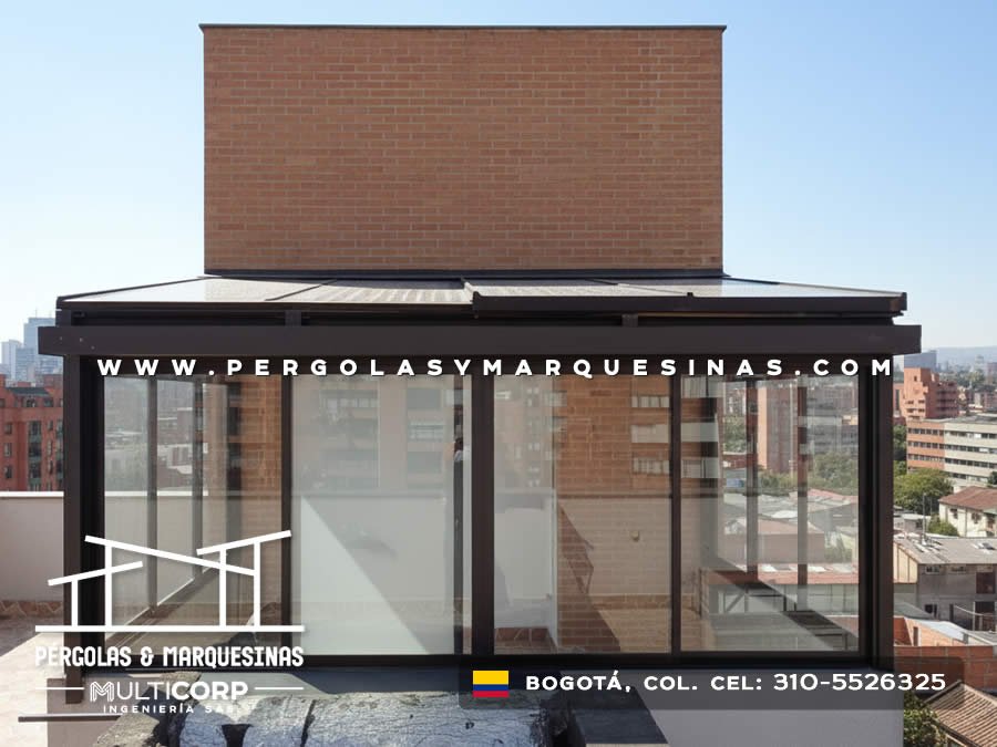 Pergola cerrada acristalada con estructura metalica oscura en terraza de atico con vista a edificios urbanos en Bogotá, Colombia. Multicorp Ingeniería SAS.