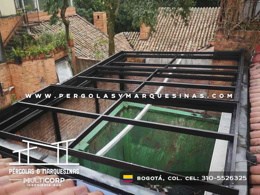 Estructura metalica oscura para cubierta de vidrio en terraza de casa con techos de tejas circunstantes en Bogotá, Colombia. Multicorp Ingeniería SAS.
