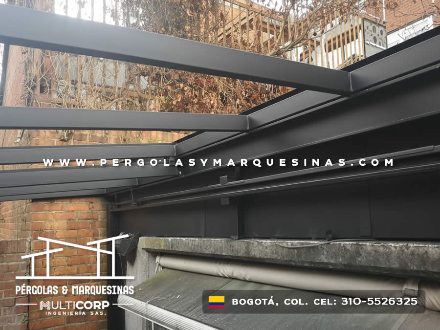 Pergola metalica oscura con perfiles retractiles en terraza de casa con muro de ladrillo en Bogotá, Colombia. Multicorp Ingeniería SAS.