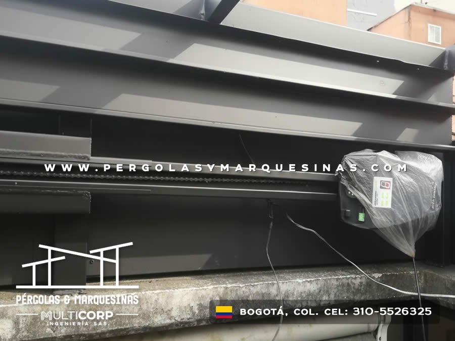 Pergola retractil metalica oscura con motor en terraza de casa con muro de ladrillo en Bogotá, Colombia. Multicorp Ingeniería SAS.