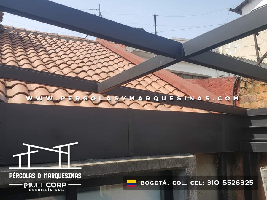 Pergola retractil metalica oscura con paneles en terraza de casa con techo de tejas circundante en Bogotá, Colombia. Multicorp Ingeniería SAS.