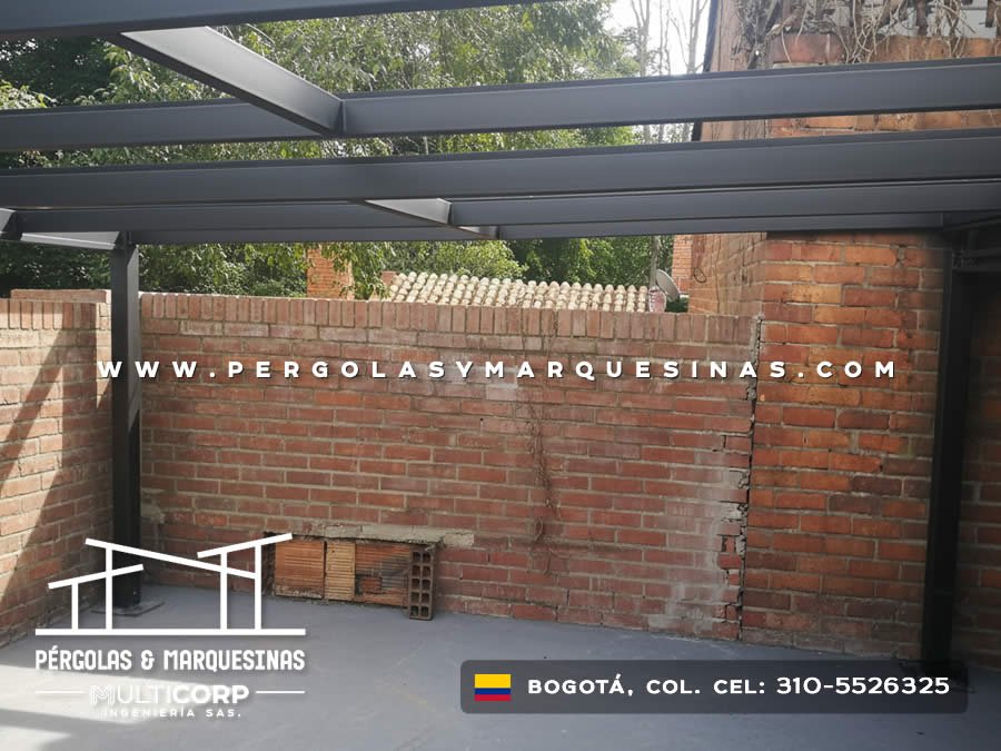 Pergola metalica oscura con perfiles horizontales en patio de casa con muro de ladrillo y vegetacion en Bogotá, Colombia. Multicorp Ingeniería SAS.