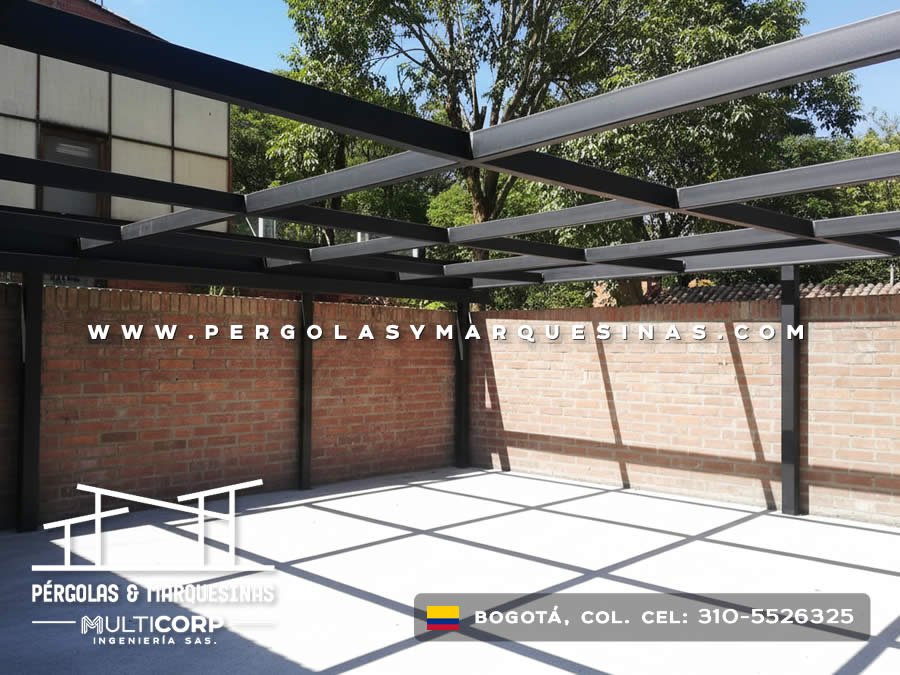 Pergola metalica oscura con perfiles en patio exterior de casa con muro de ladrillo y piso de concreto en Bogotá, Colombia. Multicorp Ingeniería SAS.