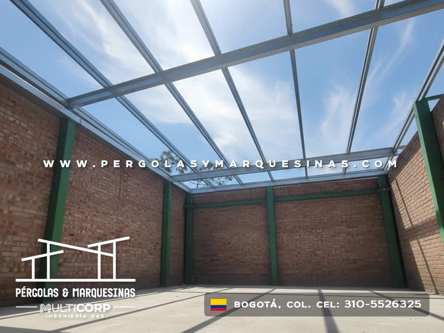 Cubierta de vidrio con estructura metalica verde en patio interior de casa con muros de ladrillo en Bogotá, Colombia. Multicorp Ingeniería SAS.