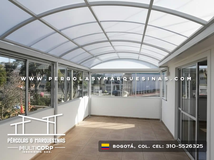 Cubierta curva de vidrio con estructura metalica blanca en terraza cerrada con vista a edificaciones urbanas en Bogotá, Colombia. Multicorp Ingeniería SAS.