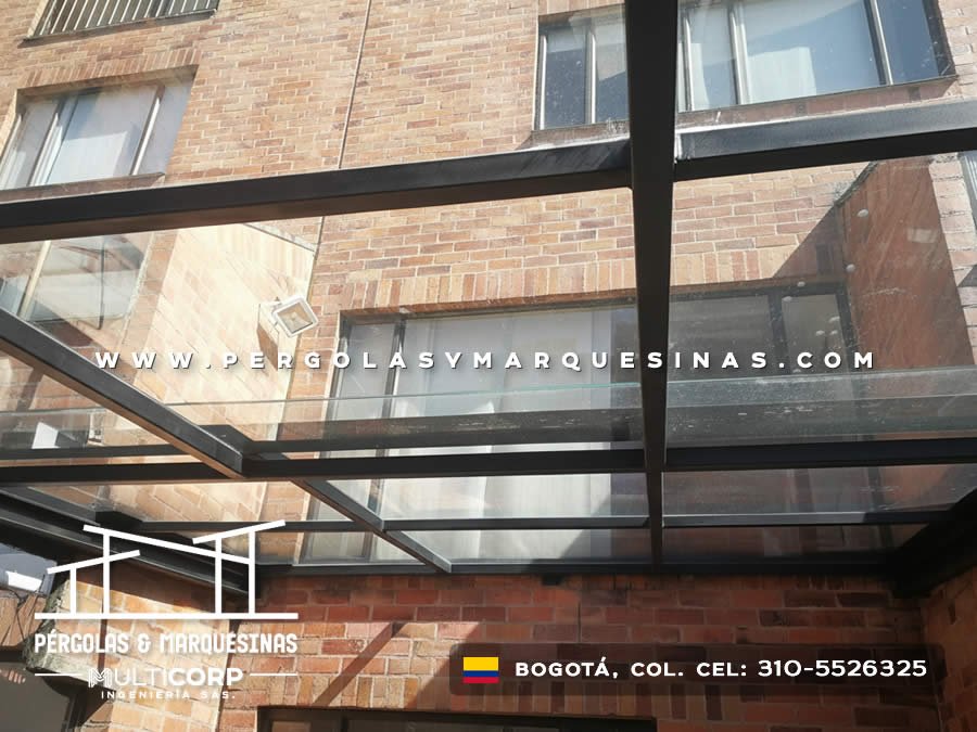 Marquesina de vidrio con estructura metalica oscura frente a fachada de ladrillo con ventanas en Bogotá, Colombia. Multicorp Ingeniería SAS.
