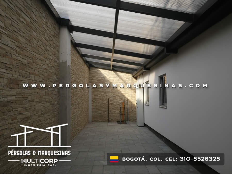 Cubierta de policarbonato con estructura metalica oscura en pasillo entre muro de piedra y pared blanca en Bogotá, Colombia. Multicorp Ingeniería SAS.