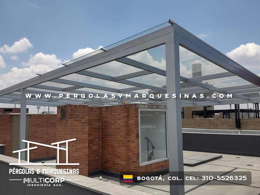 Marquesina de vidrio con estructura gris en azotea con edificio de ladrillo y skyline urbano en Bogotá, Colombia. Multicorp Ingeniería SAS.