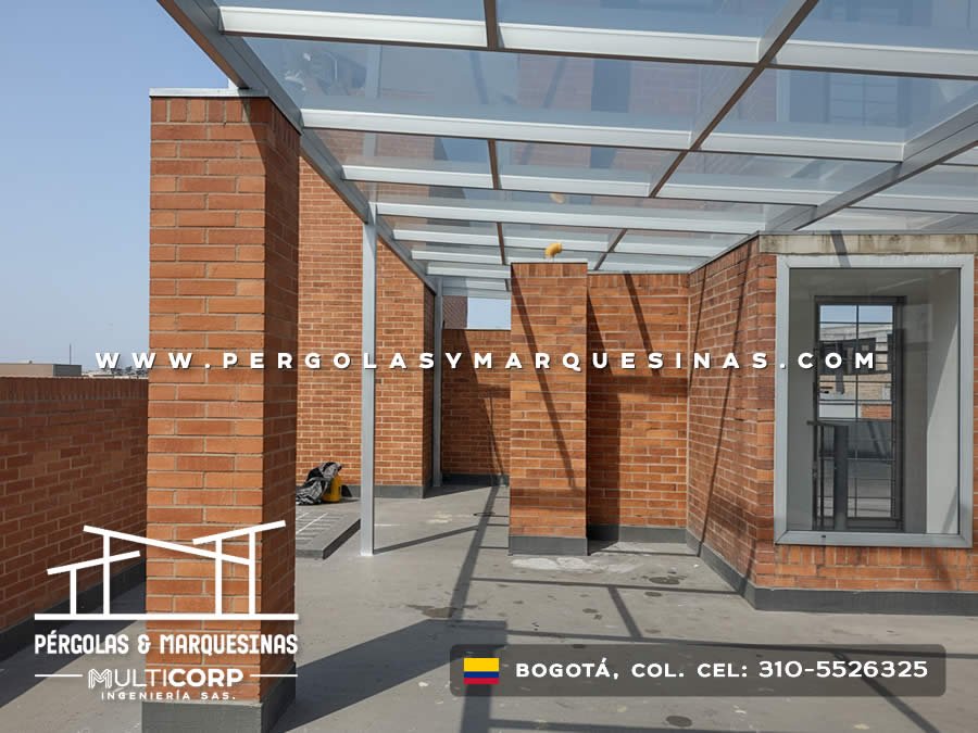 Techo de vidrio con estructura gris en azotea entre muros de ladrillo con ventanas y vista urbana en Bogotá, Colombia. Multicorp Ingeniería SAS.