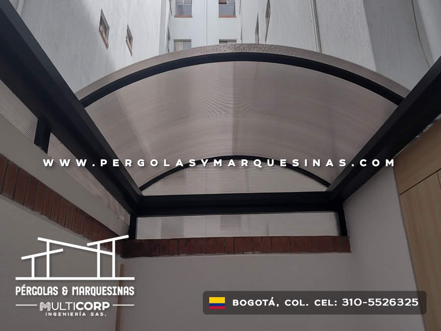Cubierta curva de policarbonato con estructura negra frente a fachada blanca de edificio en Bogotá, Colombia. Multicorp Ingeniería SAS.