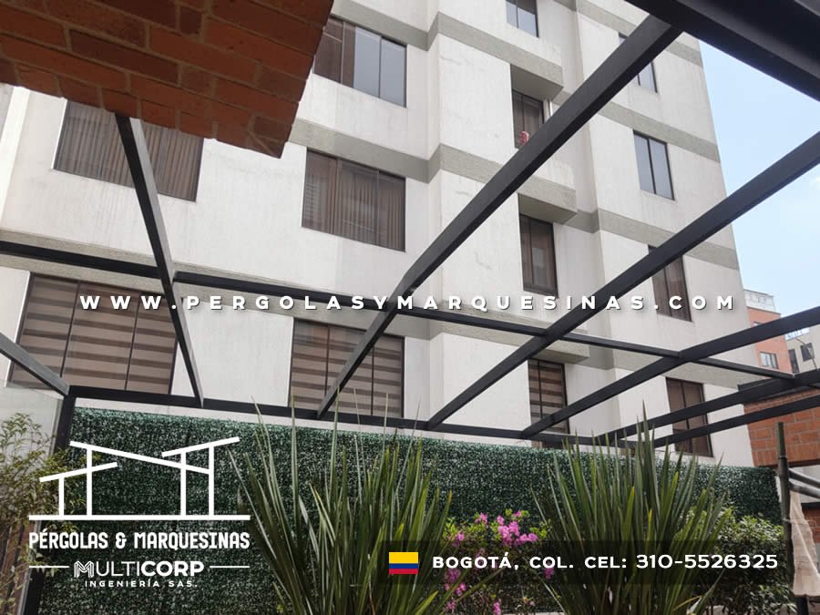 Pergola con estructura metalica negra sobre jardin vertical con plantas frente a edificio con ventanas en Bogotá, Colombia. Multicorp Ingeniería SAS.