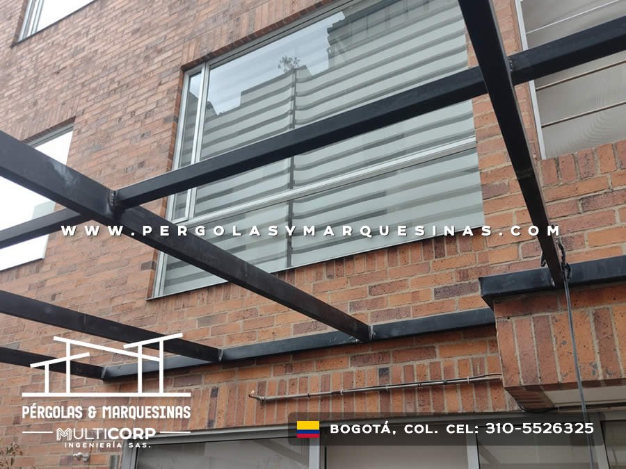 Estructura metalica negra con vidrio en entrada frente a fachada de ladrillo con ventana grande en Bogotá, Colombia. Multicorp Ingeniería SAS.