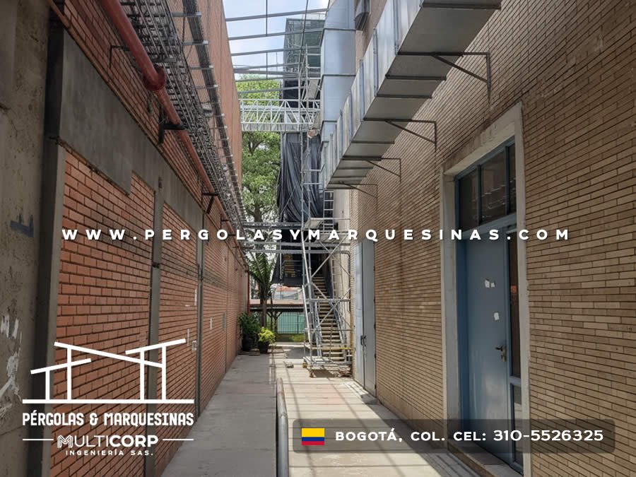 Estructura metalica en pasillo estrecho entre edificios de ladrillo con escalera y puerta azul en Bogotá, Colombia. Multicorp Ingeniería SAS.
