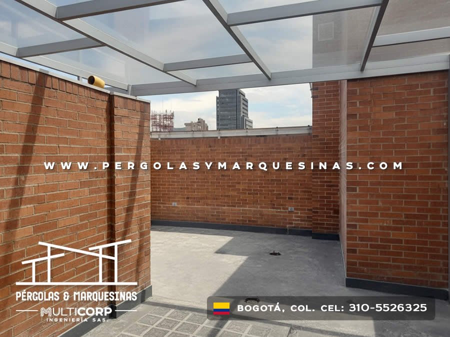Pergola con estructura gris y cubierta de vidrio en azotea moderna entre muros de ladrillo con skyline en Bogotá, Colombia. Multicorp Ingeniería SAS.