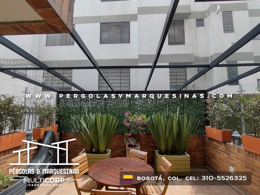 Pergola con estructura negra abierta en terraza ajardinada con mesa de madera y jardin vertical en Bogotá, Colombia. Multicorp Ingeniería SAS.