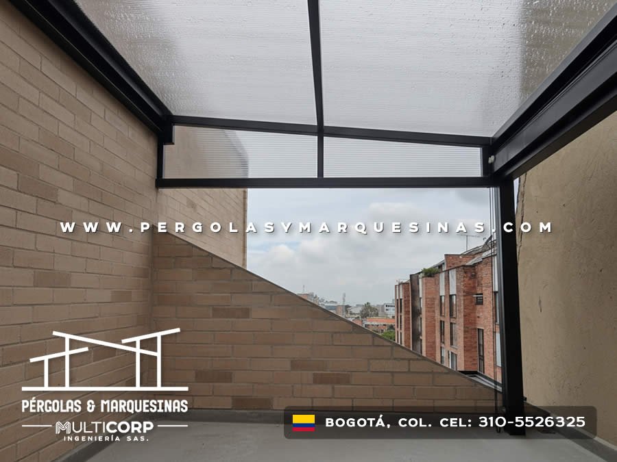 Cubierta de policarbonato con estructura oscura en terraza con muro de piedra y edificaciones urbanas en Bogotá, Colombia. Multicorp Ingeniería SAS.
