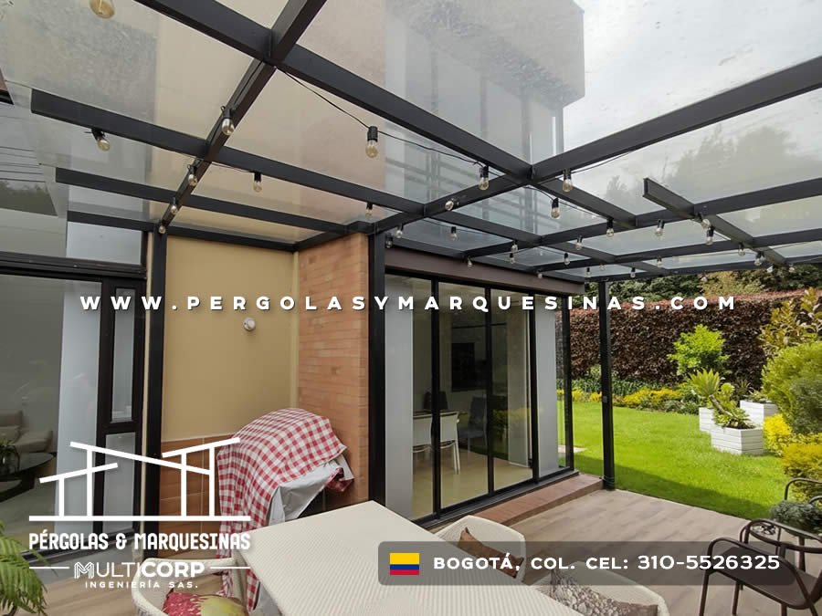 Pergola metalica oscura vidrio templado iluminacion terraza residencial jardin cesped muro verde exterior en Bogotá, Colombia. Multicorp Ingeniería SAS.