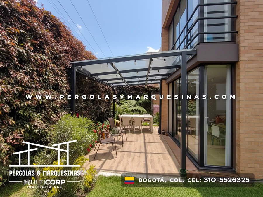 Pergola metalica oscura vidrio templado iluminacion terraza piso madera jardin cesped residencial en Bogotá, Colombia. Multicorp Ingeniería SAS.