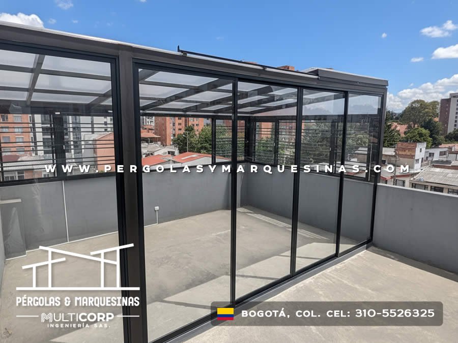 Pergola metalica negra vidrio templado terraza cerrada barandas horizontales edificios urbanos cielo azul en Bogotá, Colombia. Multicorp Ingeniería SAS.