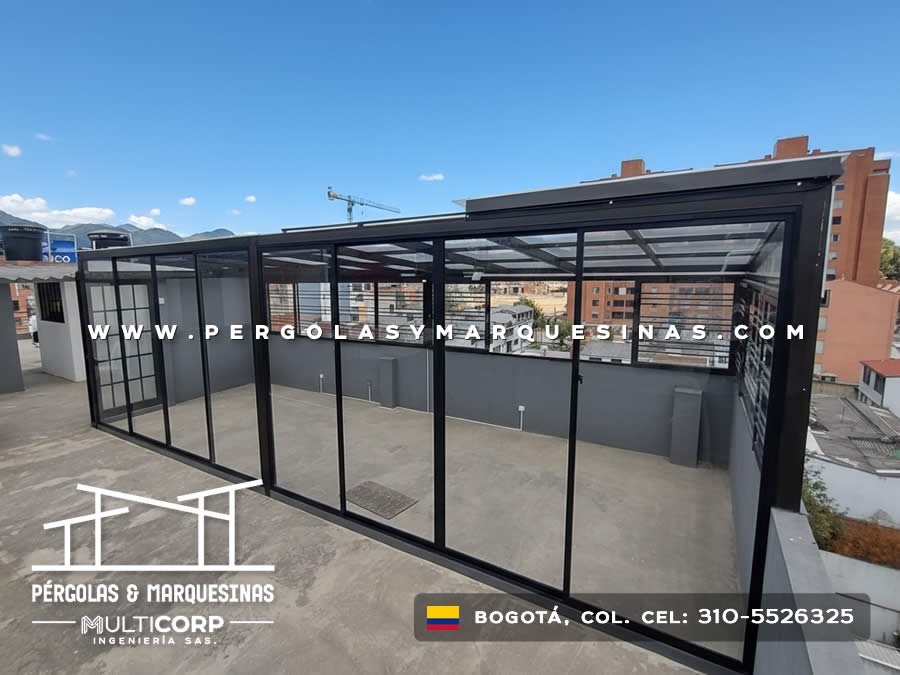 Pergola metalica negra vidrio templado terraza cerrada divisiones grua construccion edificios urbanos cielo azul en Bogotá, Colombia. Multicorp Ingeniería SAS.