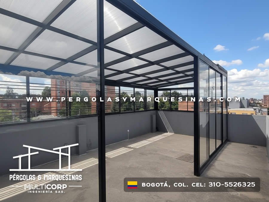Pergola metalica negra vidrio templado terraza cerrada barandas horizontales edificios urbanos cielo azul en Bogotá, Colombia. Multicorp Ingeniería SAS.